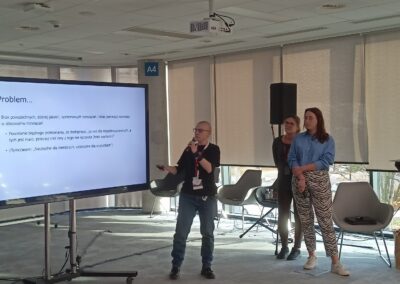 Trzy osoby na sali konferencyjnej stoją przy ekranie z wyświetloną prezentacją, omawiają projekt.