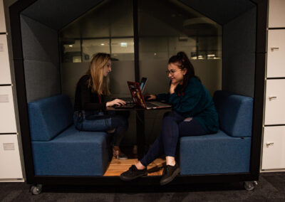 Dwie kobiety uczestniczki hackathonu siedzą przy swoich komputerach w budce wyciszającej