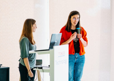 Dwie uczestniczki hackathonu stoi i przedstawia swój projekt